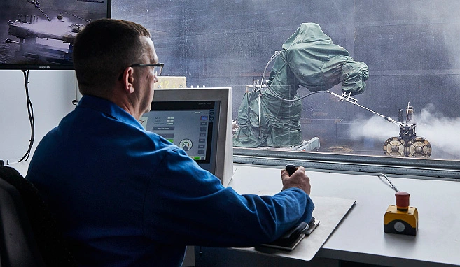 Ein BUCHEN Mitarbeiter sitzt in seinem Büro und steuert durch eine Glasscheibe hindurch den Automatisierungsroboter.